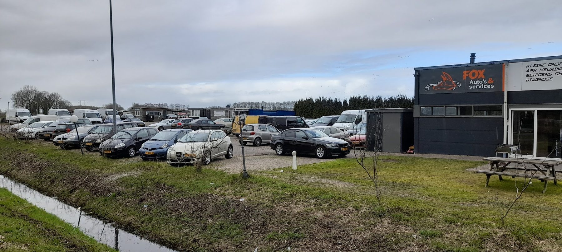 Het terrein aan de Energieweg met geparkeerde auto's en de werkplaats rechts